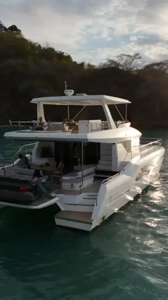 White yacht on green water beside a wooded coastline in Costa Rica